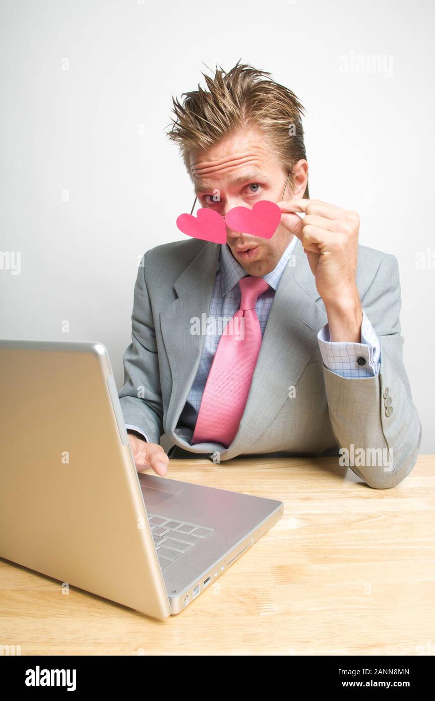 Uomo d'affari che abbassa gli occhiali rosa del cuore per avere uno sguardo più vicino al suo computer portatile Foto Stock