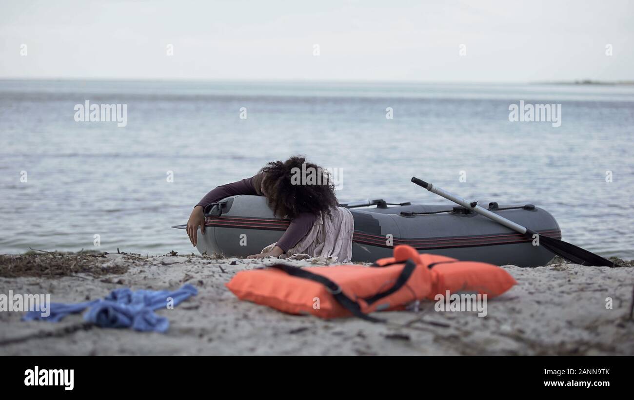 Femmina giacente sulla barca vicino alla riva del mare, giubbotto di salvataggio sul primo piano, storm vittima Foto Stock
