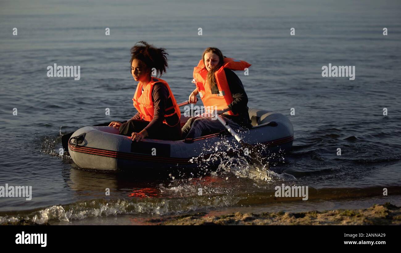 Due donne in giubbotti di salvataggio barca a remi, inondazione superstiti in cerca di aiuto a terra Foto Stock