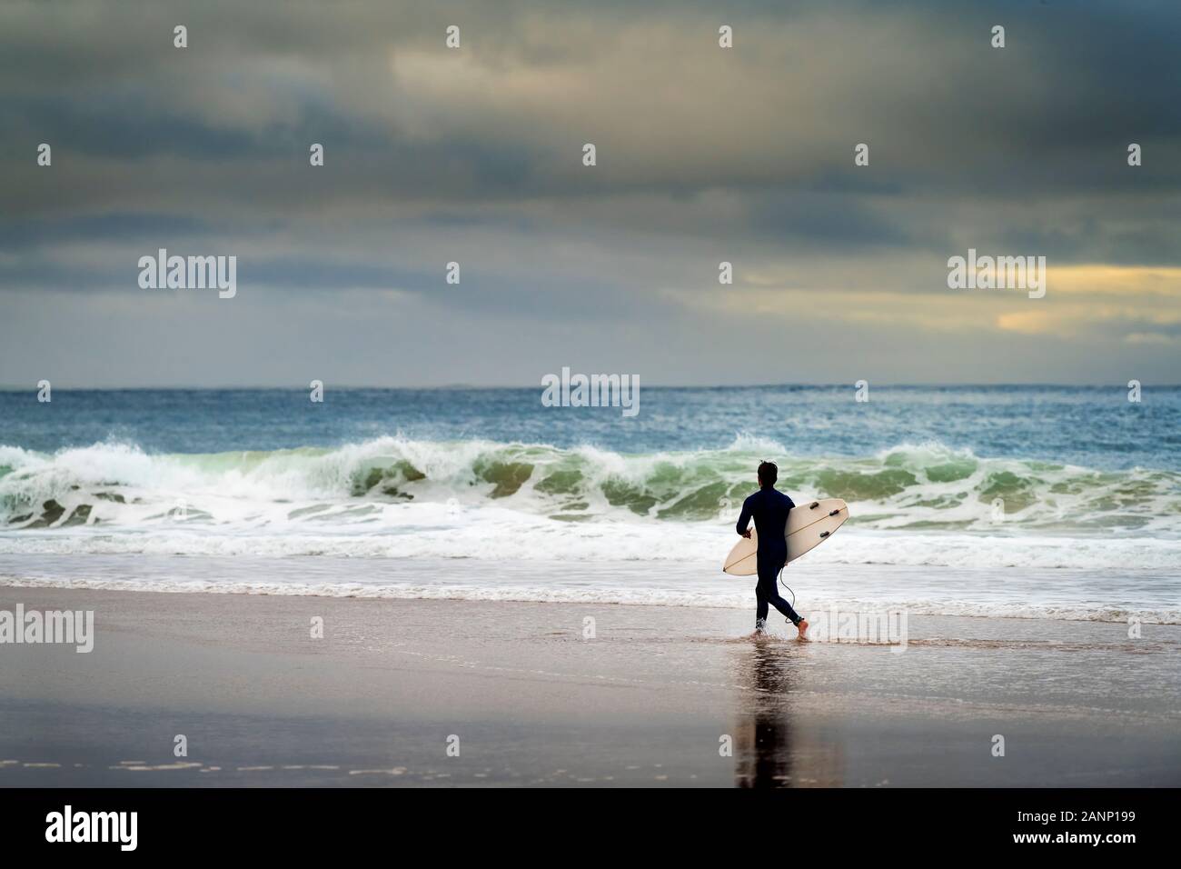 Un surfista che entra in mare presso la spiaggia di Carcavelos a Oeiras, in Portogallo Foto Stock