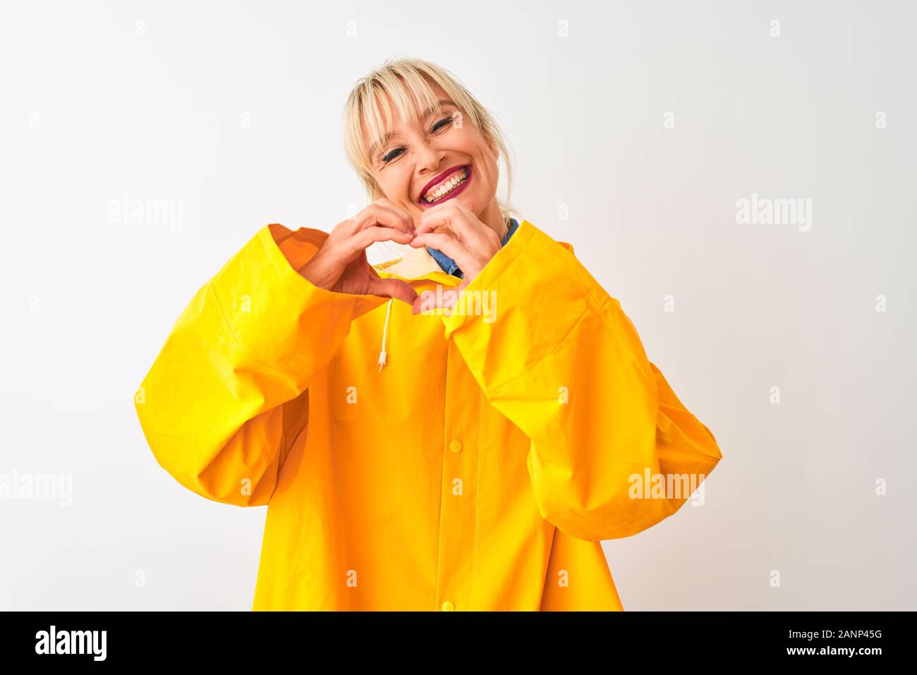 Medioevo donna che indossa il giallo cappotto di pioggia in piedi isolato su sfondo bianco sorridente in amore che mostra il simbolo del cuore e la forma con le mani. Romantico Foto Stock