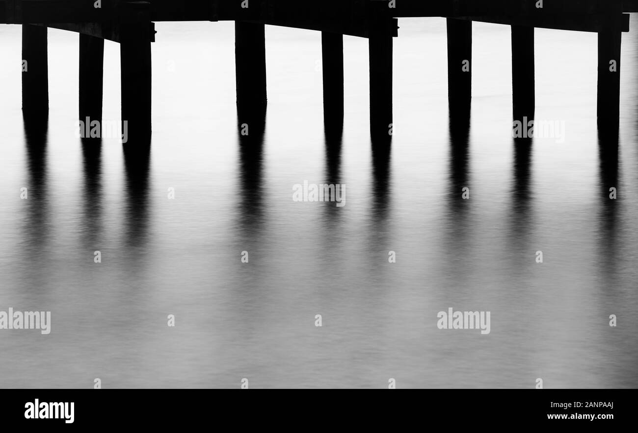 Foto minimalista di pier e tralicci e acqua vicino al tramonto, realizzata utilizzando una lunga esposizione Foto Stock