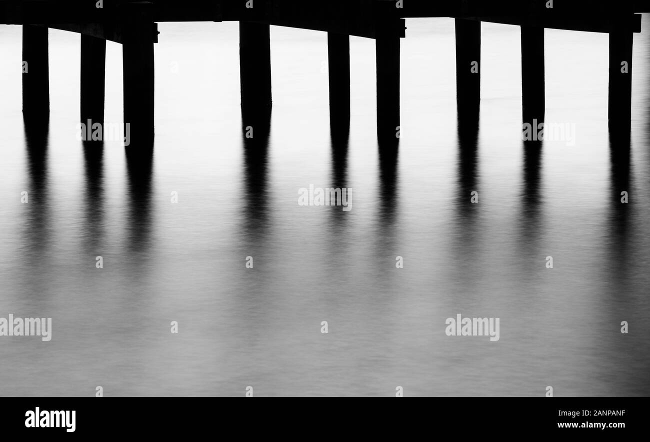 Foto minimalista di pier e tralicci e acqua vicino al tramonto, realizzata utilizzando una lunga esposizione Foto Stock