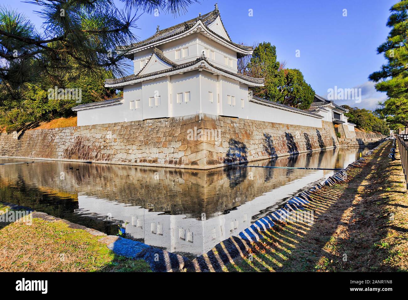 Angolo bianco torre di avvistamento di Kyoto il castello Nijo - Palazzo del shogunato giapponese. Morbida luce mattutina che riflette ancora in acque di fossato circostante. Foto Stock