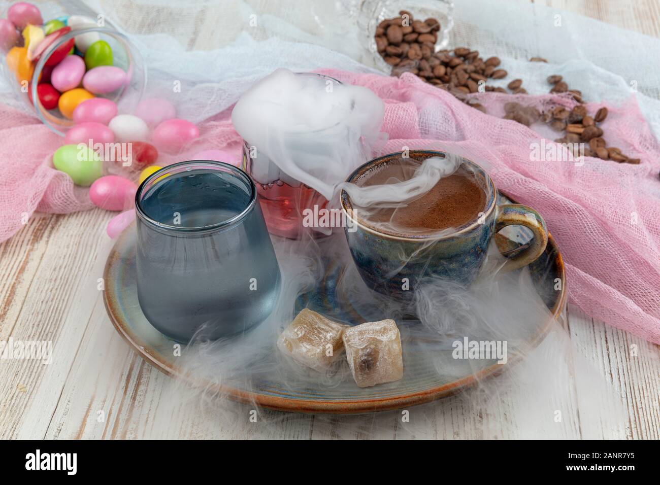 Turca tradizionale caffè nella tazza di porcellana impostare,un bicchiere di acqua e delizie turche e colorati di mandorla caramelle sulla superficie con i chicchi di caffè. Una festa (f Foto Stock