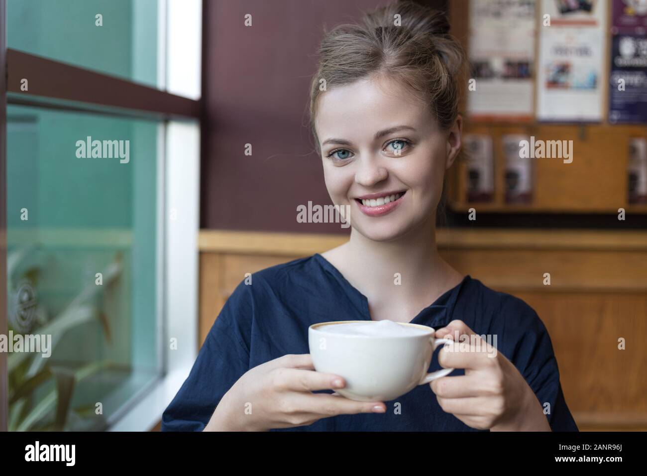 Bella ragazza caucasica sorridente giovane ragazza tenendo una tazza bianca di caffè in un bar, ristorante Foto Stock