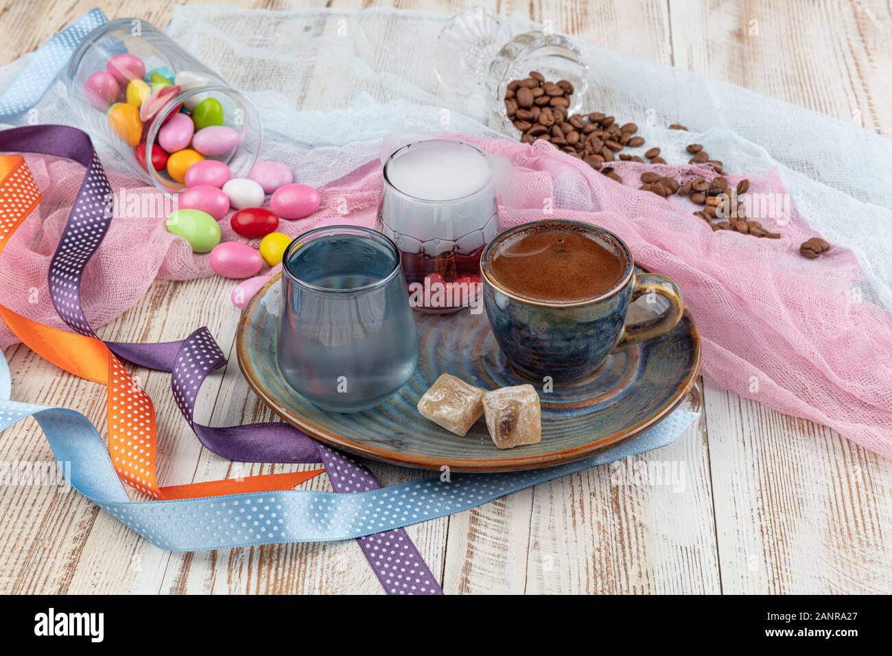 Turca tradizionale caffè nella tazza di porcellana impostare,un bicchiere di acqua e delizie turche e colorati di mandorla caramelle sulla superficie con i chicchi di caffè. Una festa (f Foto Stock