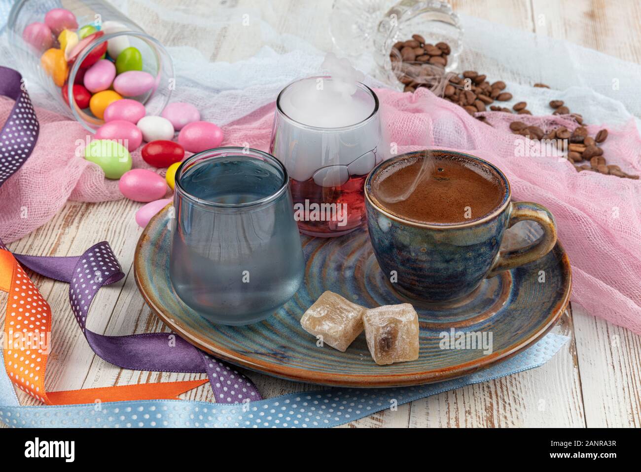 Turca tradizionale caffè nella tazza di porcellana impostare,un bicchiere di acqua e delizie turche e colorati di mandorla caramelle sulla superficie con i chicchi di caffè. Una festa (f Foto Stock