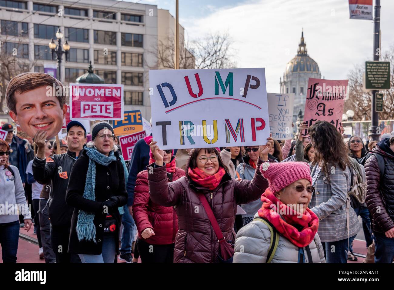 San Francisco, Stati Uniti d'America. 18 gennaio, 2020. La quarta edizione di donne di Marzo a San Francisco, California. Una folla di contestatori marzo giù Market Street di San Francisco in background. Dimostranti portano i segni della lettura, 'Dump Trump " e " le donne per Pete' tra gli altri. Una vecchia donna indossa un rosa pussy hat in primo piano. Foto Stock