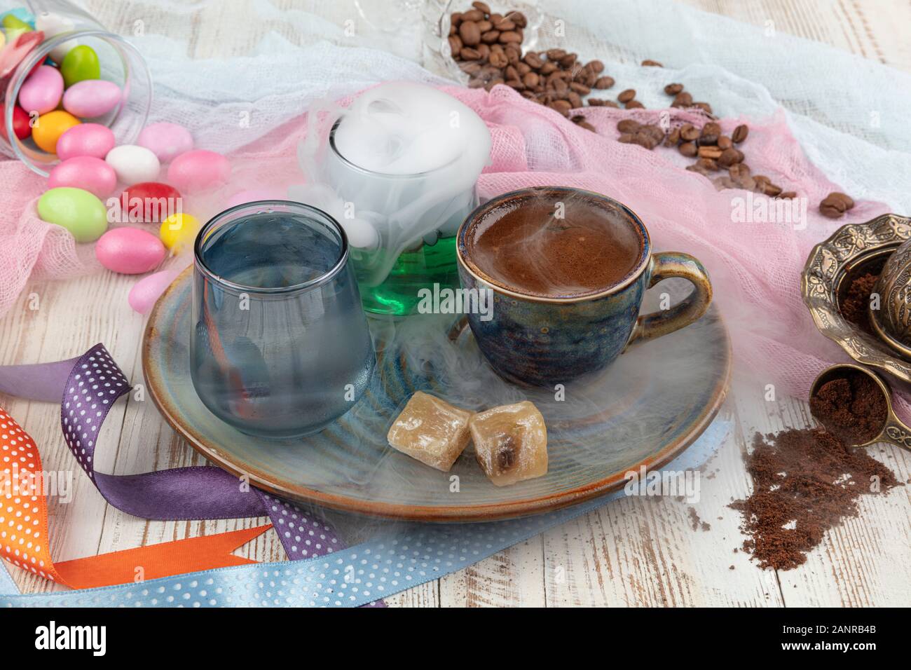 Turca tradizionale caffè nella tazza di porcellana impostare,un bicchiere di acqua e delizie turche e colorati di mandorla caramelle sulla superficie con i chicchi di caffè. Una festa (f Foto Stock