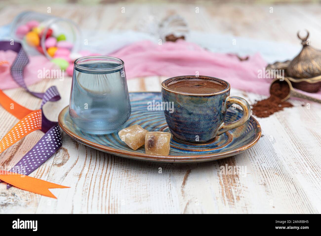 Turca tradizionale caffè nella tazza di porcellana impostare,un bicchiere di acqua e delizie turche e colorati di mandorla caramelle sulla superficie con i chicchi di caffè. Una festa (f Foto Stock