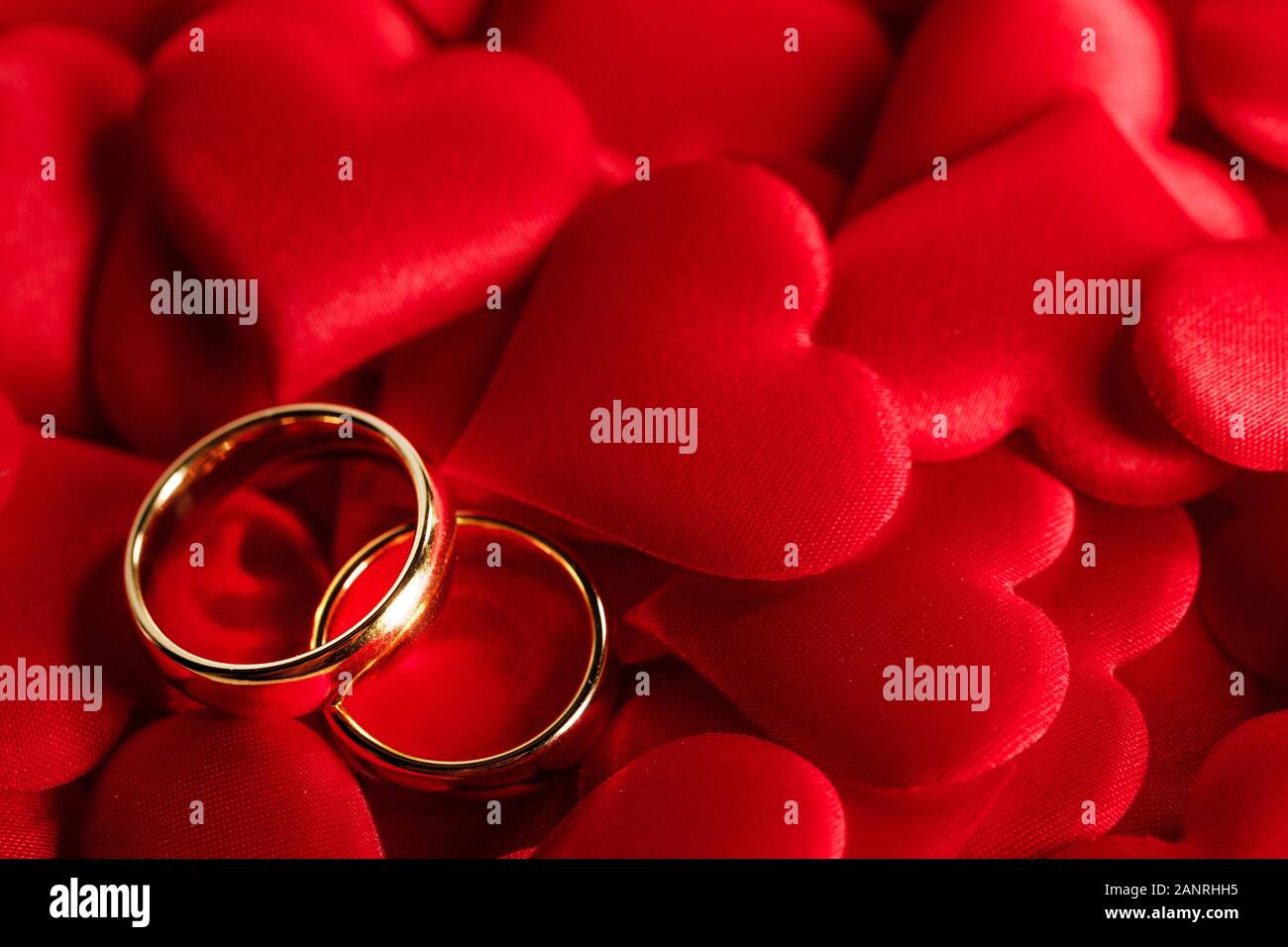 Due anelli da sposa dorati su sfondo rosso satinato cuori Foto Stock