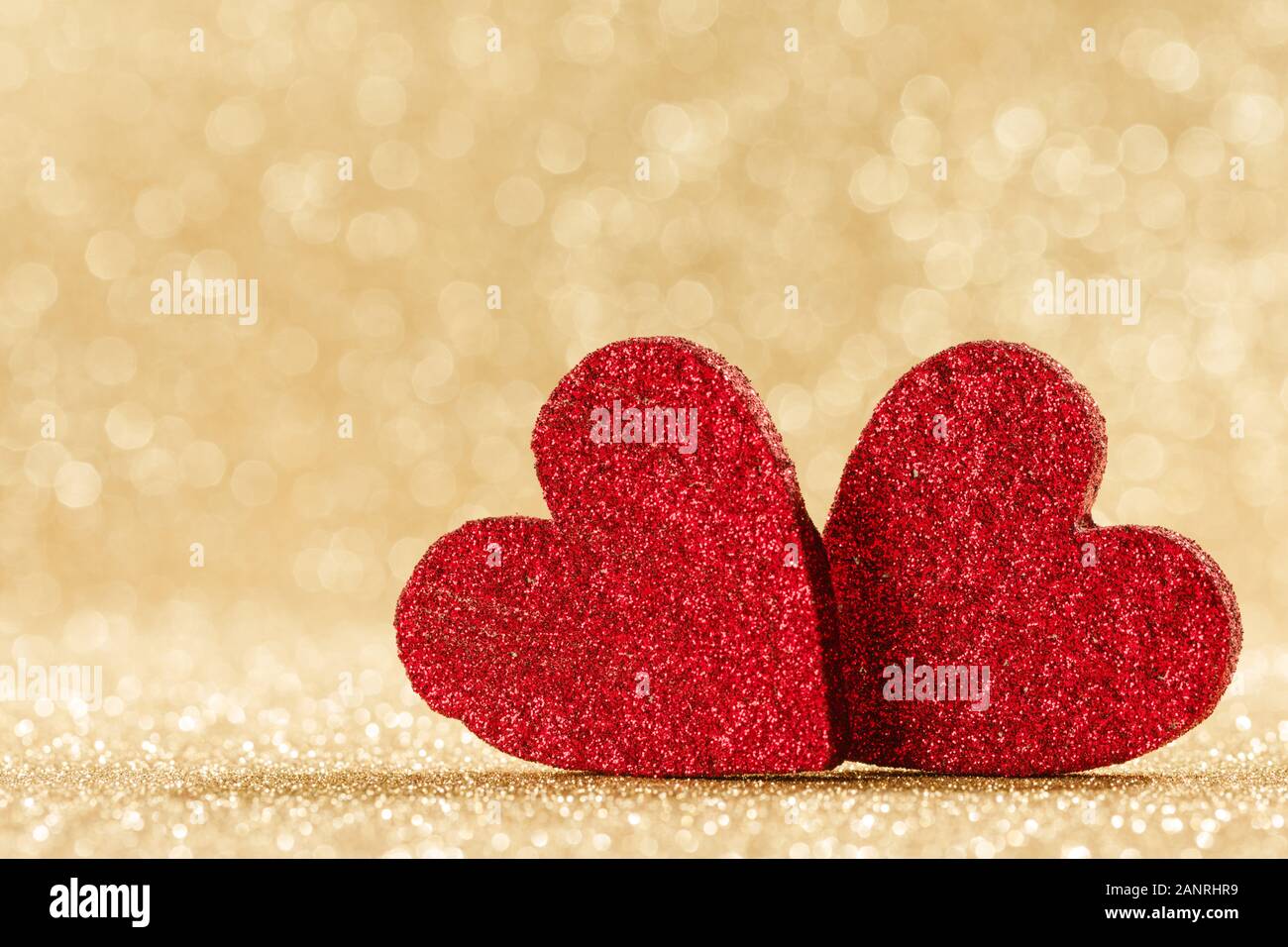 Due piccoli fatti a mano glitter rosso cuori in bright golden lights sfondo bokeh Valentines Day card Foto Stock