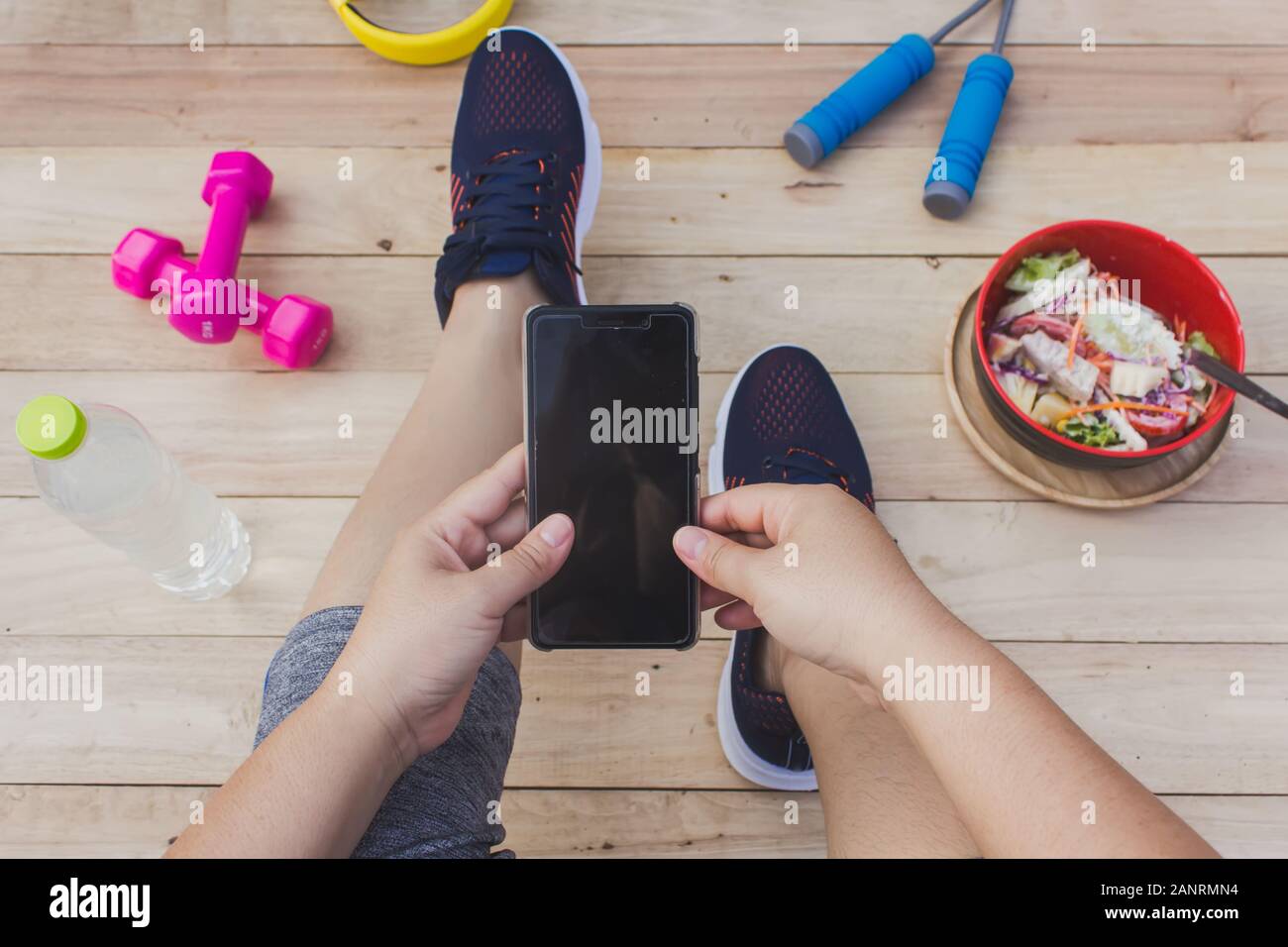 La ragazza possiede un telefono cellulare con attrezzature per esercizi, un pavimento in legno. Foto Stock