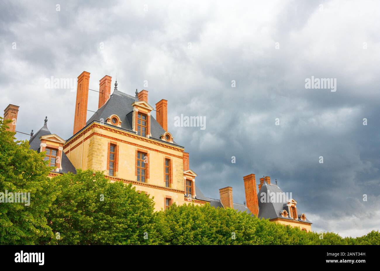 Vista dell'edificio Cour des Offices, parte del Castello di Fontainebleau, sotto un cielo nuvoloso drammatico. Francia. Foto Stock