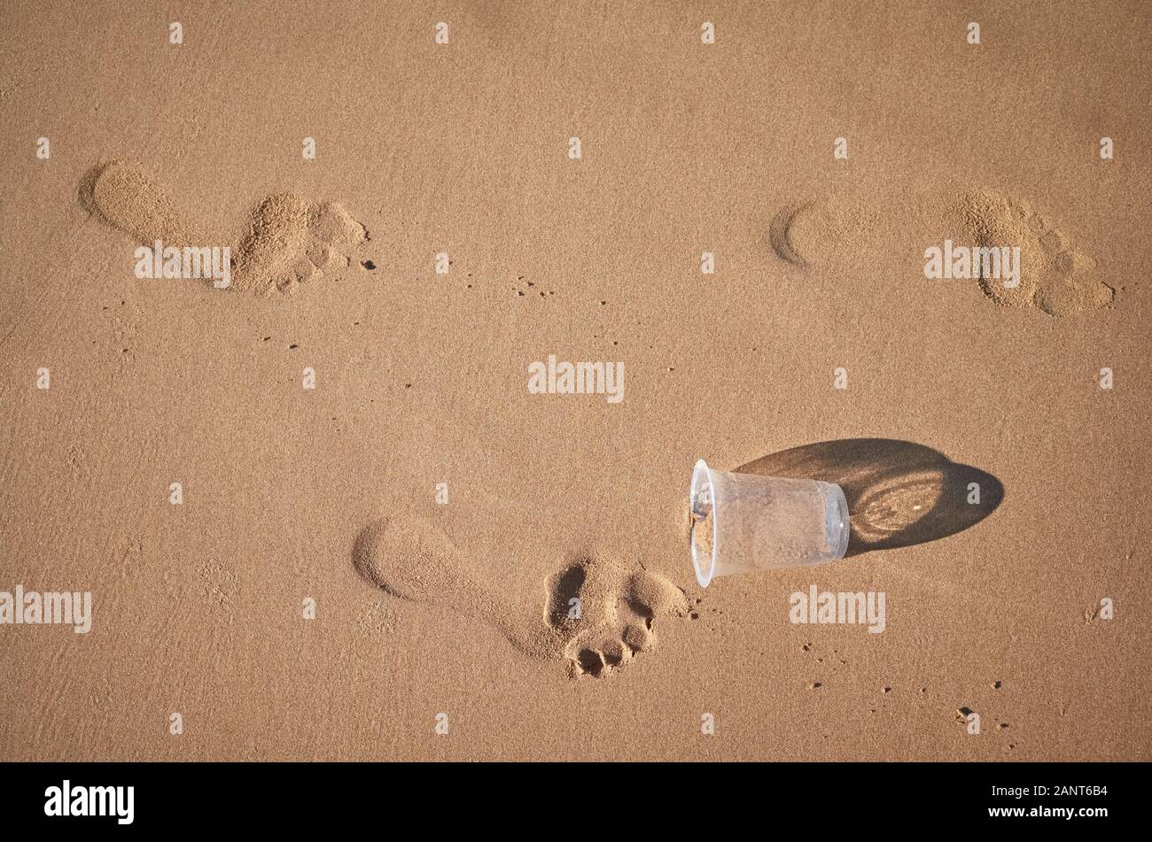 Footprint e bicchiere di plastica su di una spiaggia di sabbia, quadro concettuale. Foto Stock
