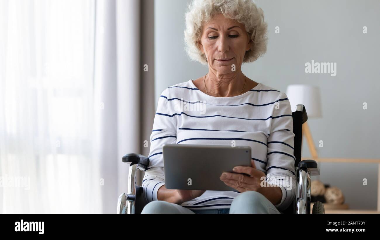 Donna anziana seduta in carrozzina tramite computer tablet Foto Stock