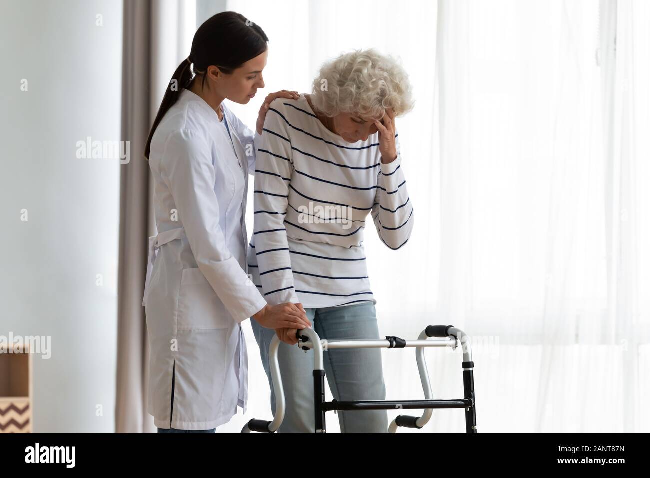 Il caregiver aiutare anziani disabili donna in piedi con walker, senso di malessere Foto Stock