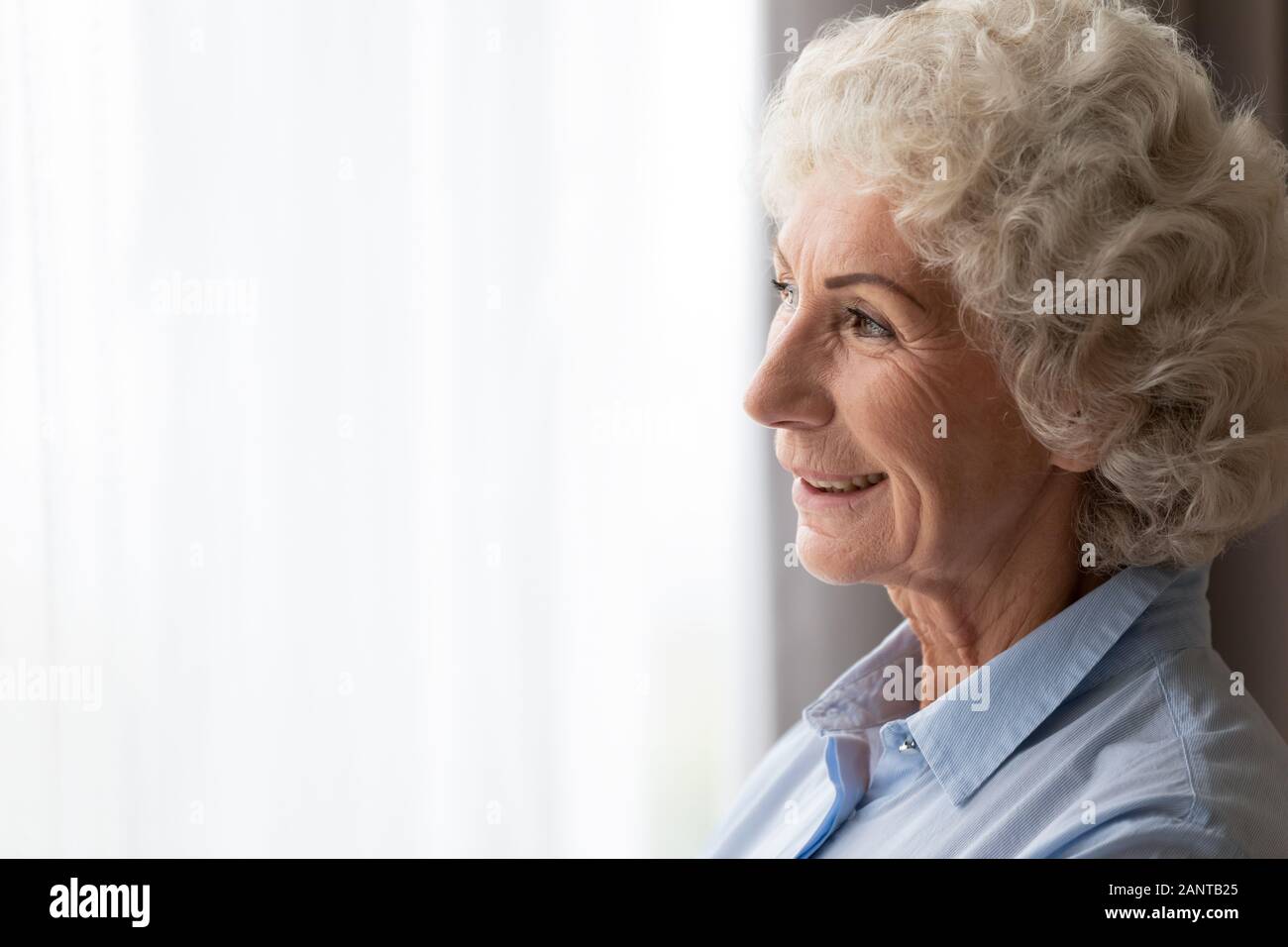 Close up felice donna sorridente a guardare fuori dalla finestra, sognare da soli Foto Stock