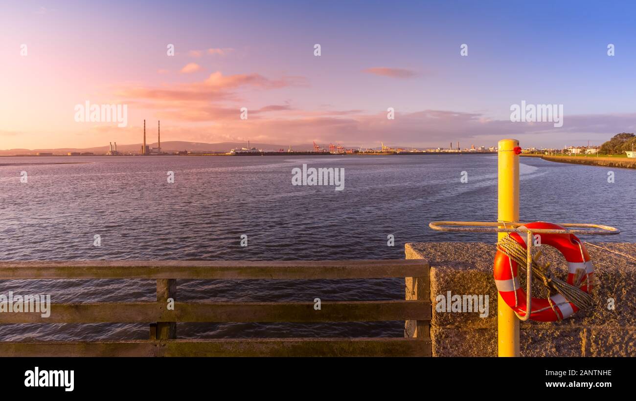 Vista sul porto di Dublino con Poolbeg Power Plant, alte ciminiere e gru di banchina da Bull Island. Salvagente in primo piano. Incredibile sunrise, Irlanda Foto Stock