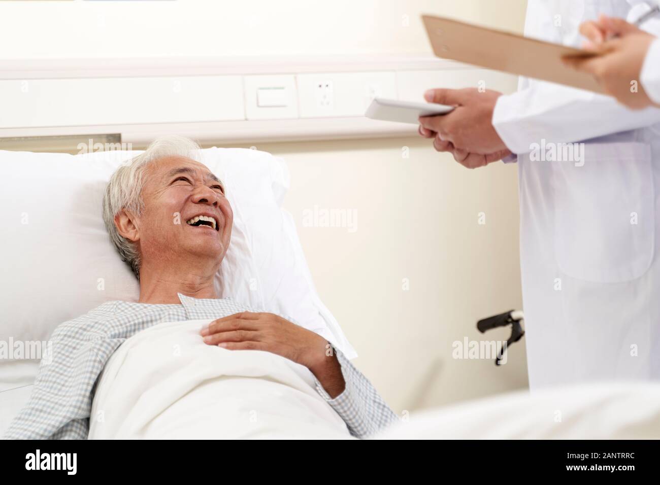 Felice asian vecchio uomo disteso nel letto di ospedale a parlare con i medici Foto Stock