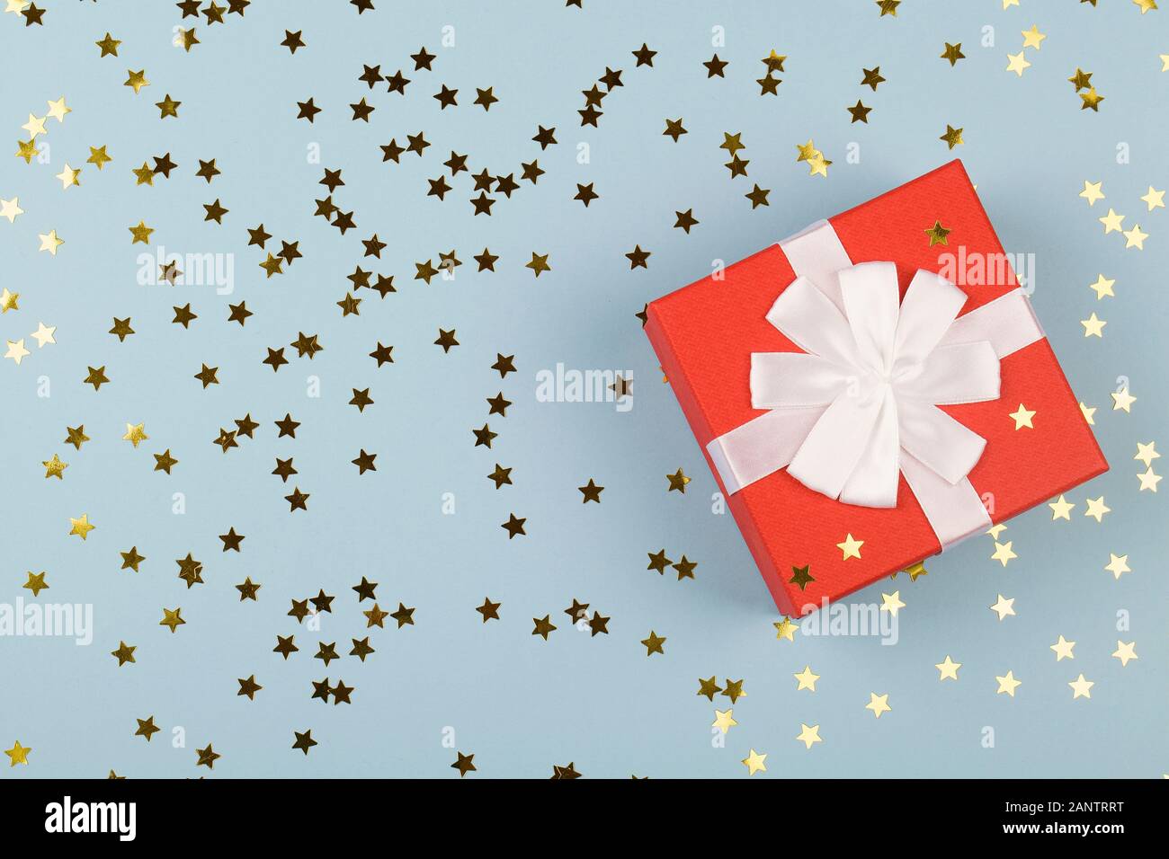 Scatola regalo rossa con nastro bianco su sfondo blu con piccole stelle. Chiudere lo spazio di copia della vista superiore. Foto Stock