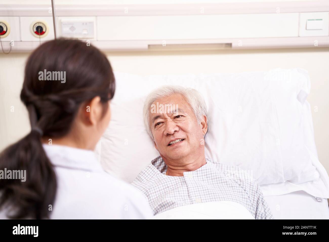 Giovani asiatici medico parlando a senior paziente al posto letto in ospedale Foto Stock