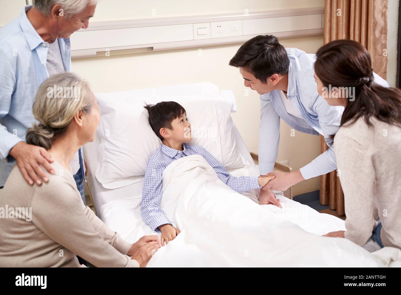 Cinque anni bambino asiatico che giace nel letto di ospedale riceve una visita da genitori e nonni Foto Stock