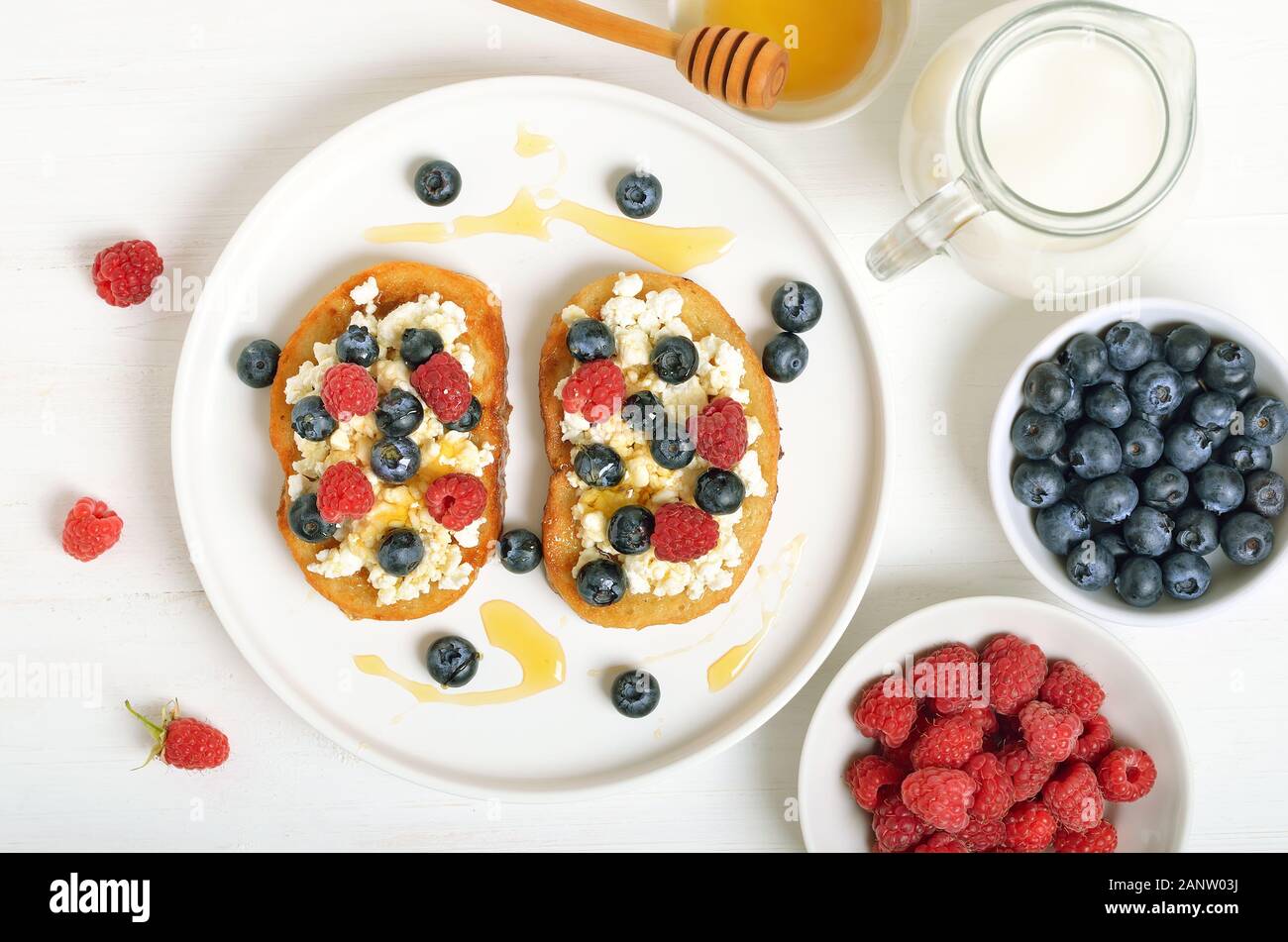 Panini con formaggio spalmabile, mirtilli e lamponi e miele sulla piastra bianca. Lamponi freschi e mirtilli nella ciotola. Vista superiore, laici piatta Foto Stock