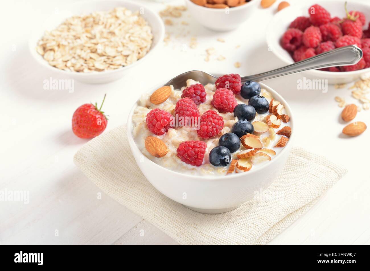 Una sana prima colazione. Farina di avena porridge con lamponi mirtilli e i dadi nella ciotola sul tavolo bianco Foto Stock