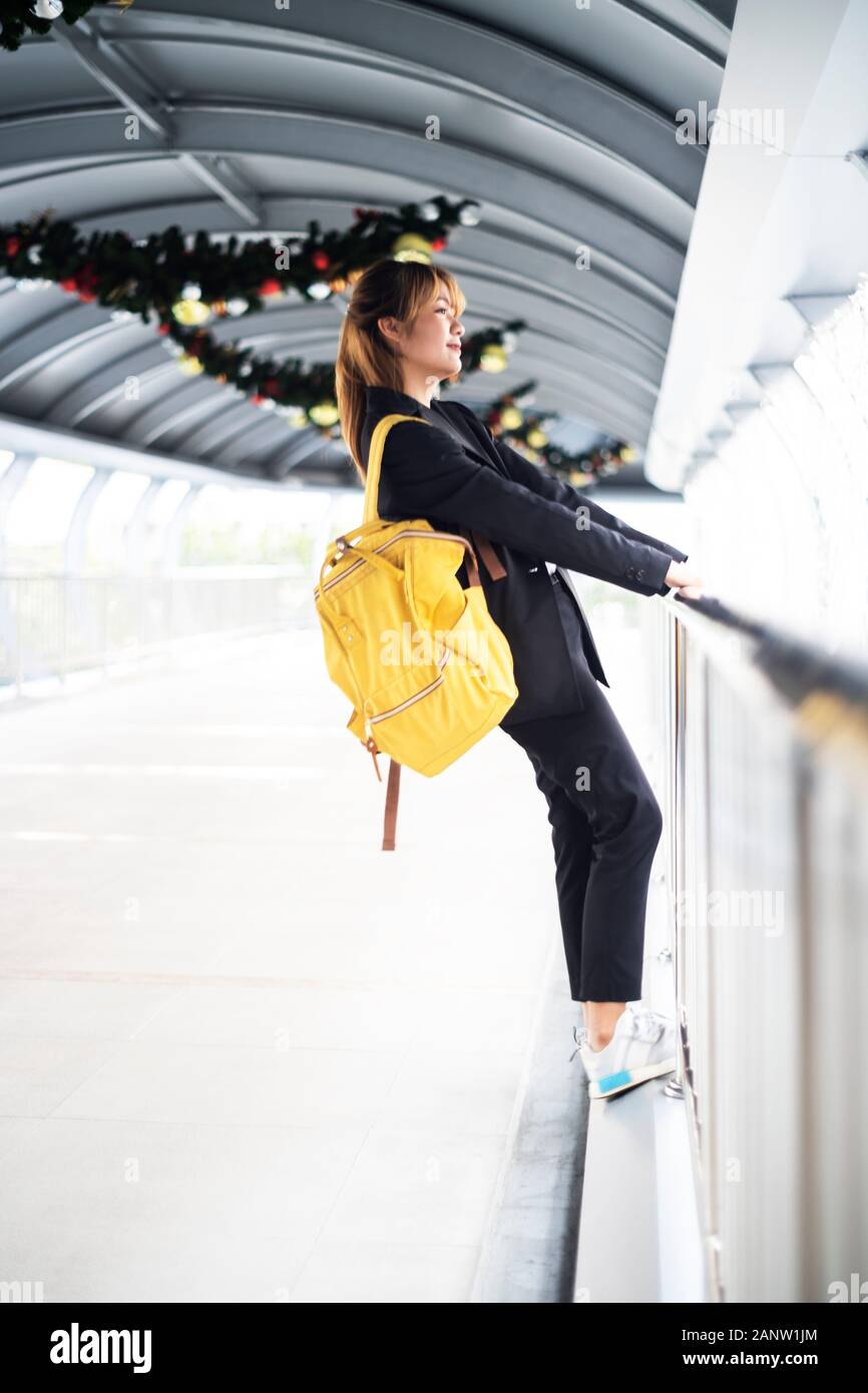 Capelli biondi donna vestiti di nero tenere premuto fino al corrimano su skywalk e rilassatevi con la felicità come un divertimento kid. Foto Stock