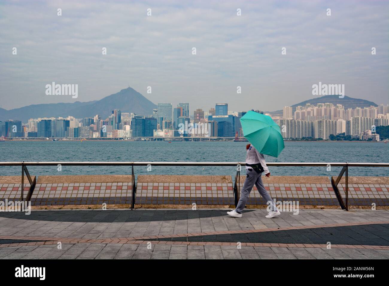 Una donna con un ombrello cammina sulla passeggiata di Quarry Bay sul lungomare di Victoria Harbour a Hong Kong. Foto Stock