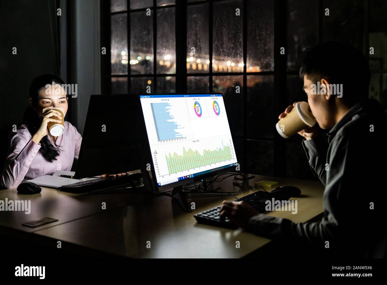 Giovane adulto uomo d'affari asiatici e la donna a bere il caffè caldo mentre si lavora a tarda notte nel loro ufficio con computer desktop e laptop. Utilizzo come disco Foto Stock