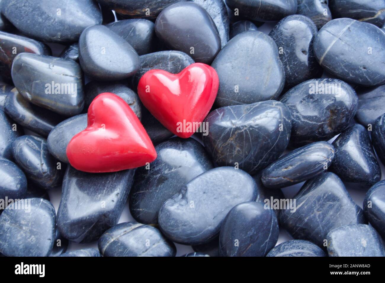 Due cuori rossi su ciottoli neri sfondo. Foto Stock