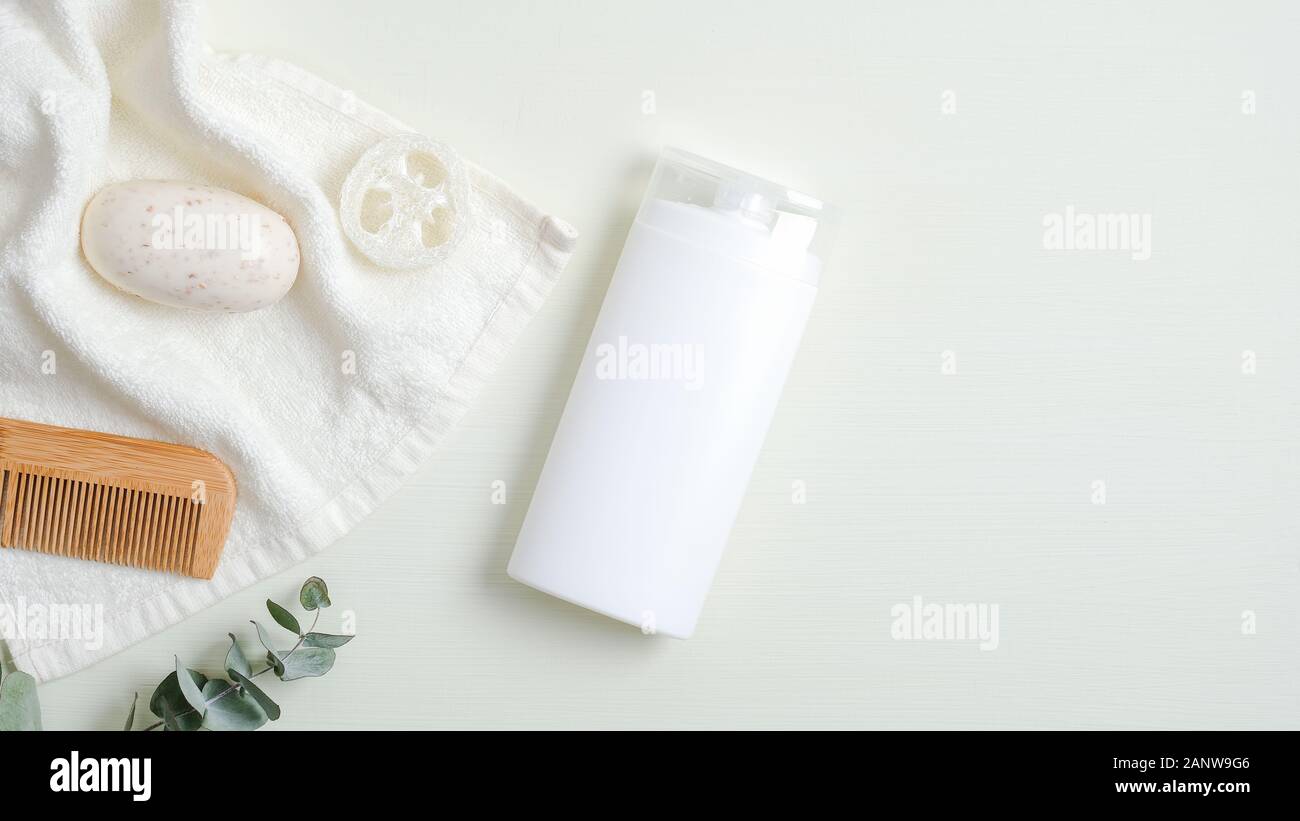 Cura dei capelli concetto di design. SPA bottiglia cosmetici imballaggi in legno Pettine per capelli, asciugamano bianco, sapone organico, spugna Luffa su sfondo verde. Valori minimi Foto Stock