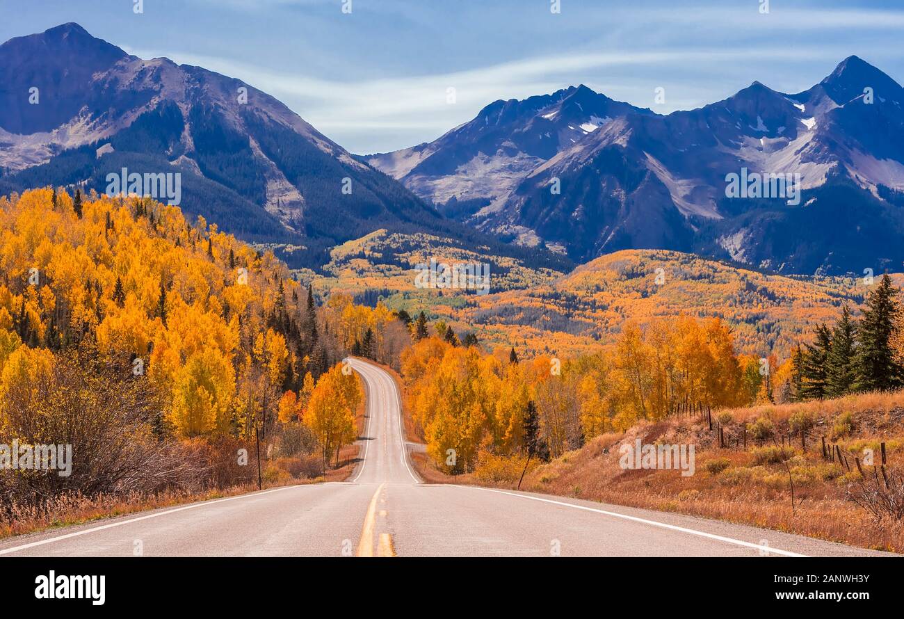 Un vuoto di Colorado Highway 145 nel mezzogiorno circondato da Autunno a colori nei pressi di Telluride, Colorado. Foto Stock