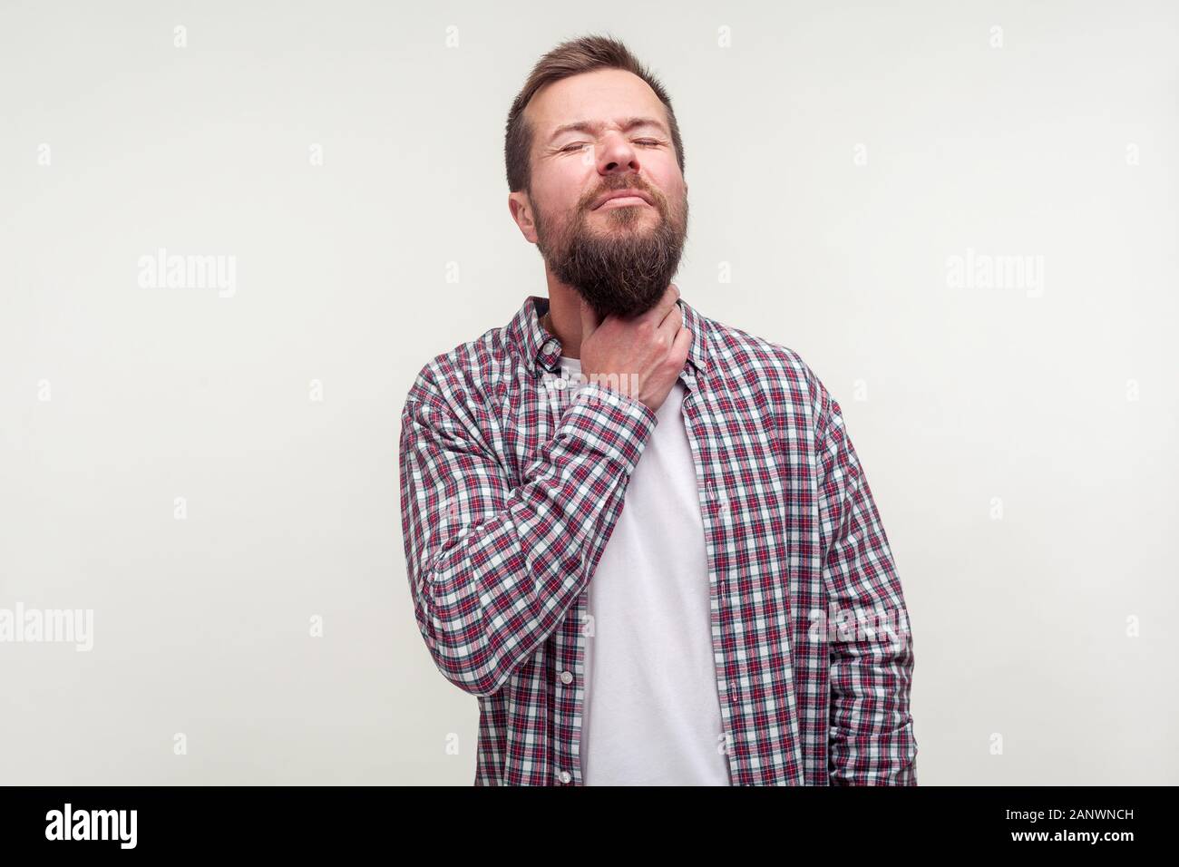 I sintomi di influenza. Ritratto di malati uomo barbuto in casuale plaid shirt toccando il collo sofferenza mal di gola, duro da digerire, chiudendo gli occhi in grimace di inte Foto Stock