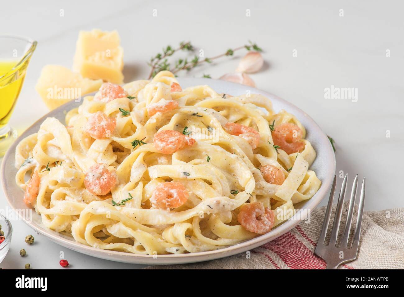 La pasta italiana Le fettuccine con gamberi in una salsa cremosa con parmigiano e timo in una piastra su marmo bianco tavola. close up Foto Stock