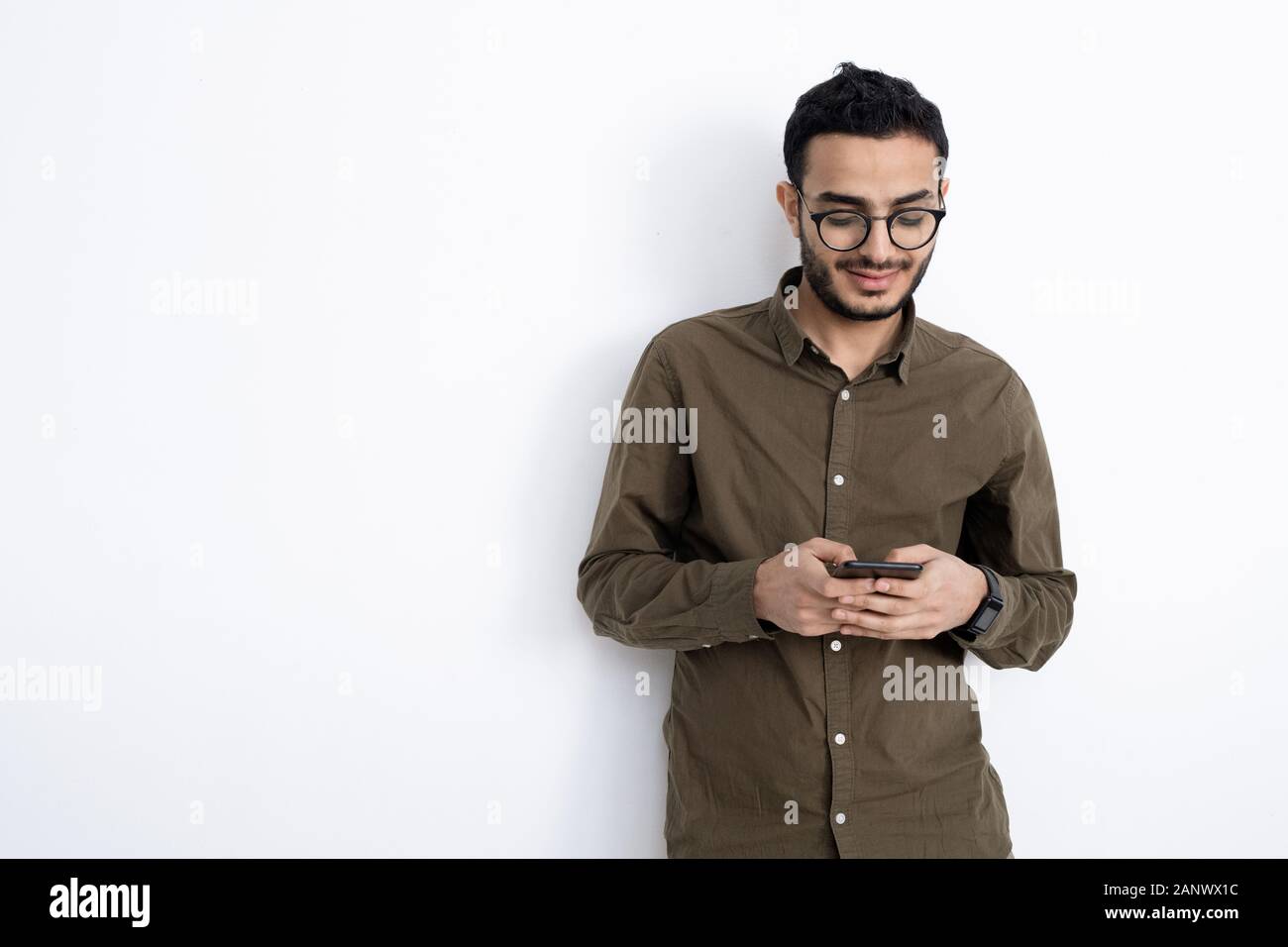 Giovane imprenditore sorridente in occhiali e camicia in piedi da muro bianco Foto Stock