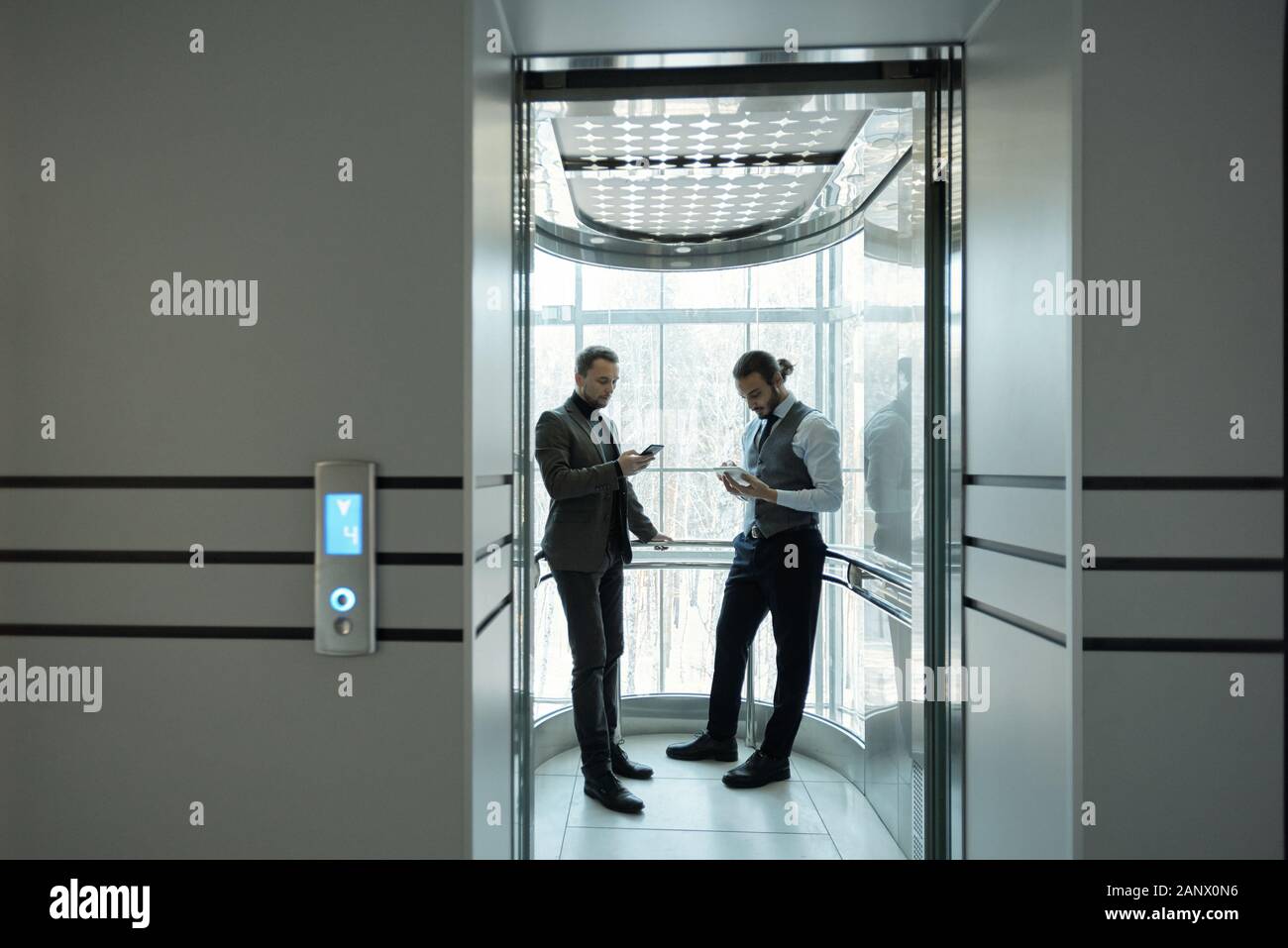 Due giovani ben vestito imprenditori maschio utilizzando mobile gadget in ascensore Foto Stock
