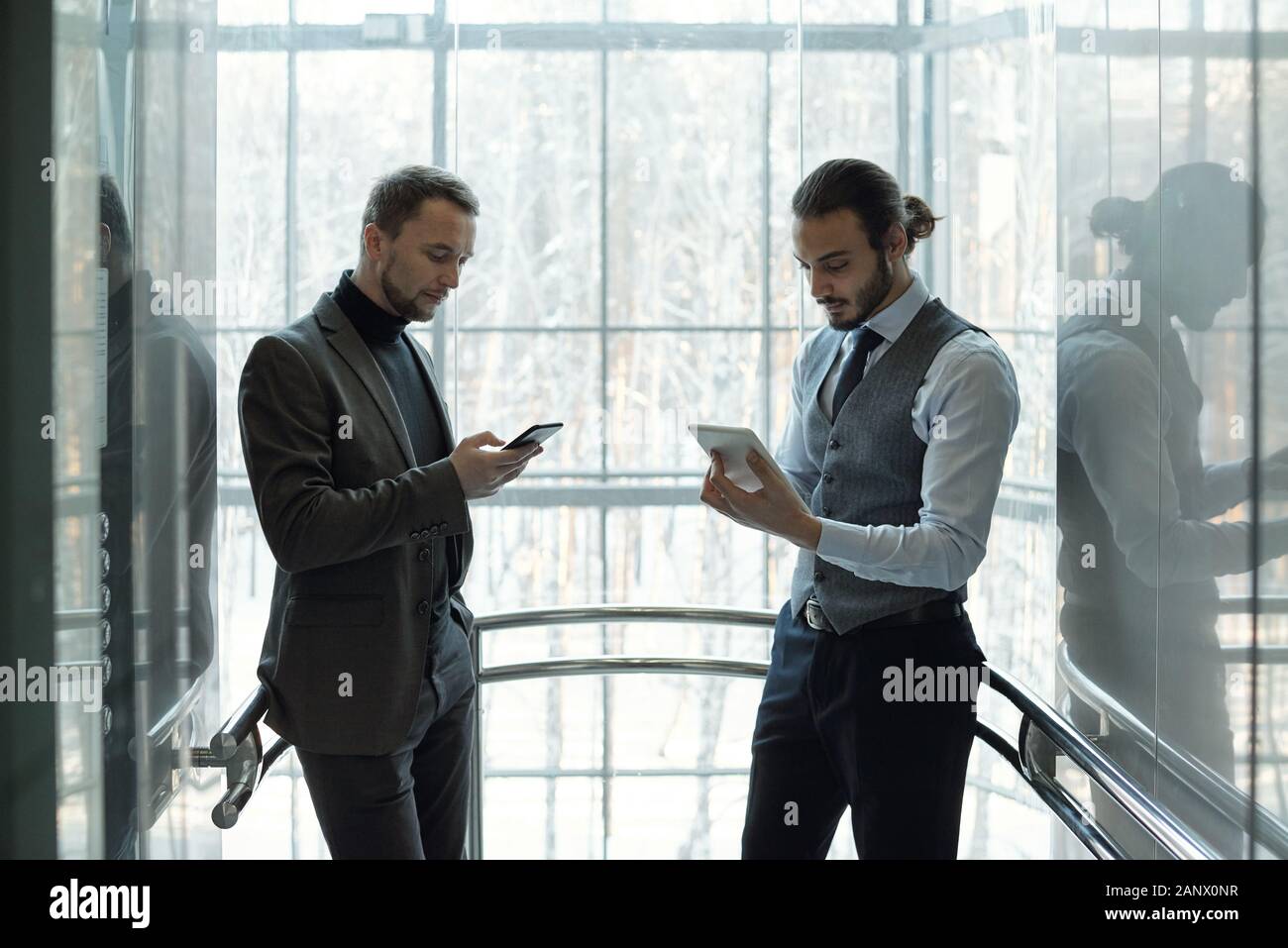 Due giovani ben vestito imprenditori utilizzando mobile gadget a rottura Foto Stock