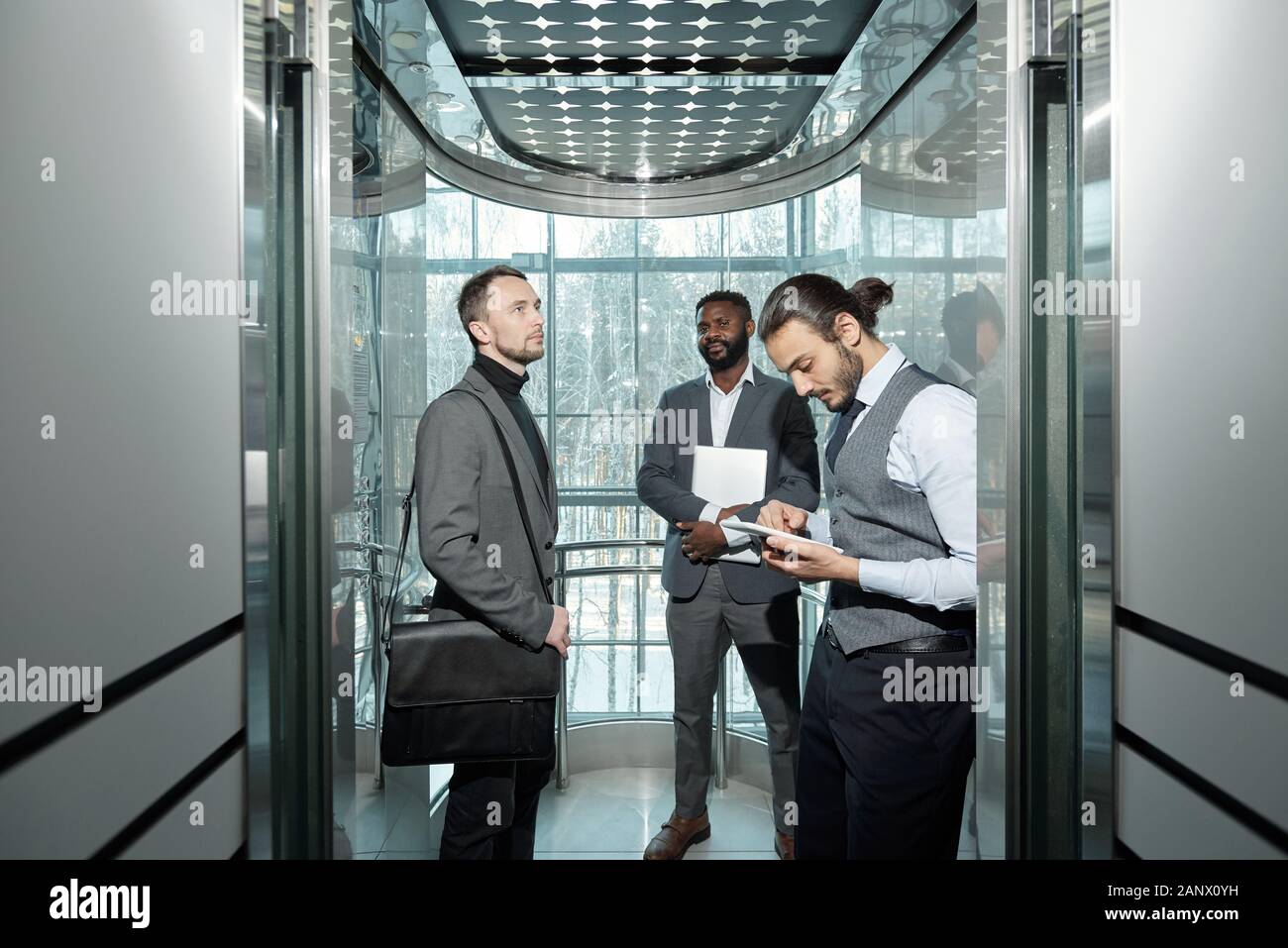 I giovani ben vestito imprenditore maschio utilizzando digitale compressa in ascensore Foto Stock