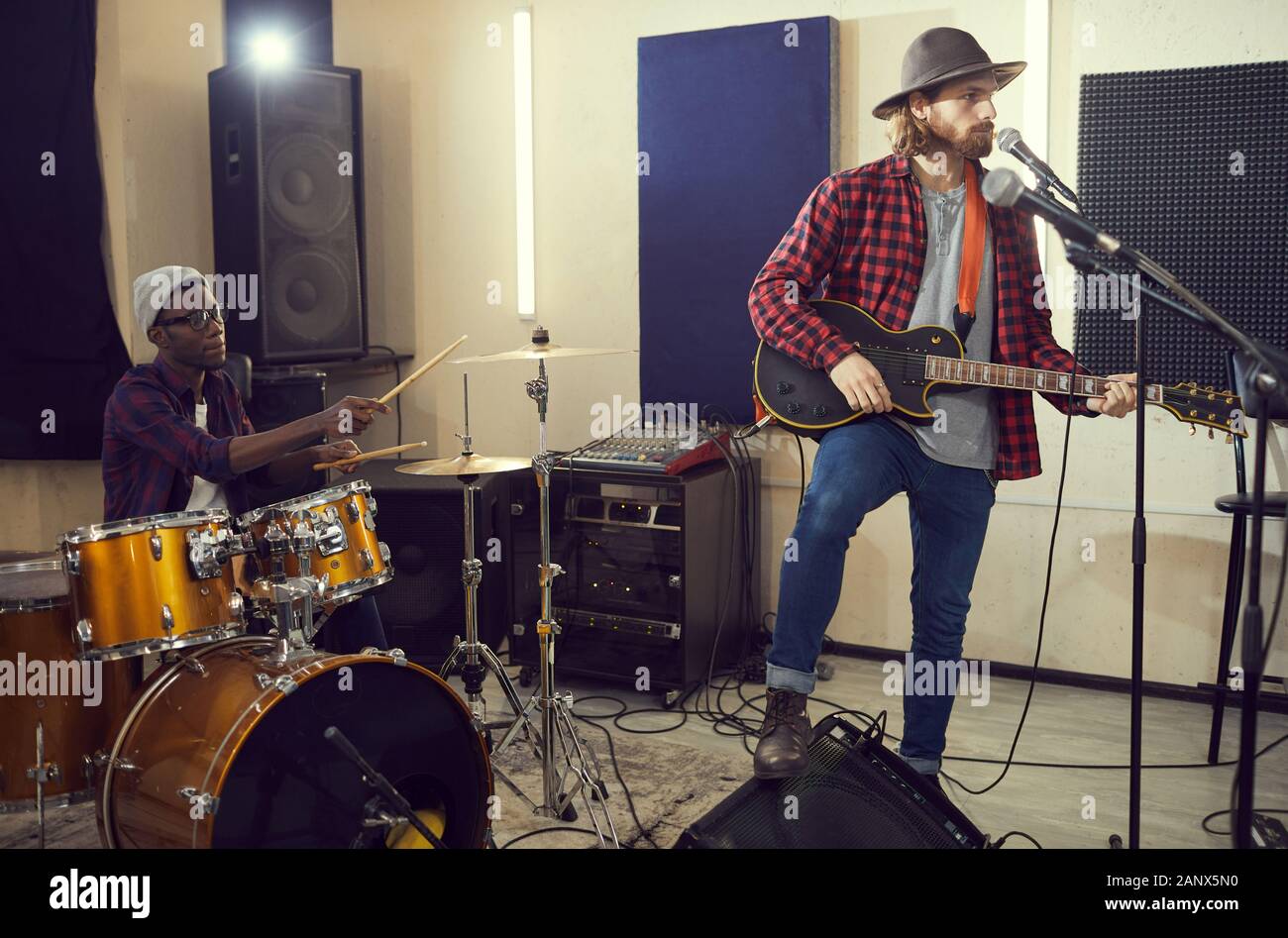 A piena lunghezza Ritratto di bello con i capelli lunghi uomo cantano al microfono durante le prove o di concerto con la banda musicale, spazio di copia Foto Stock