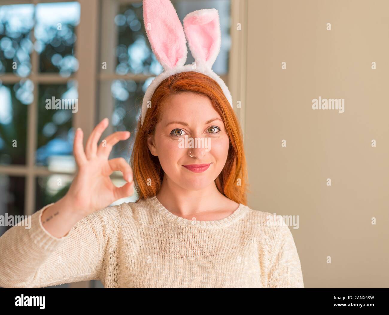 Redhead donna che indossa la pasqua orecchie di coniglio a casa facendo  segno ok con le dita, simbolo eccellente Foto stock - Alamy