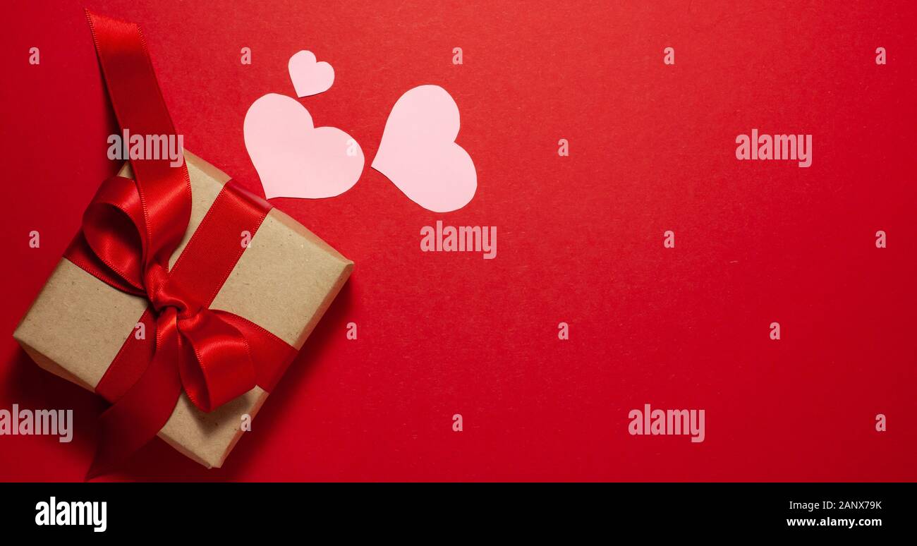 Cuori rosa di diverse dimensioni in prossimità della carta marrone confezione regalo con un nastro rosso bow. Il giorno di San Valentino del concetto. Flat Top laici vista con spazio per il testo su r Foto Stock