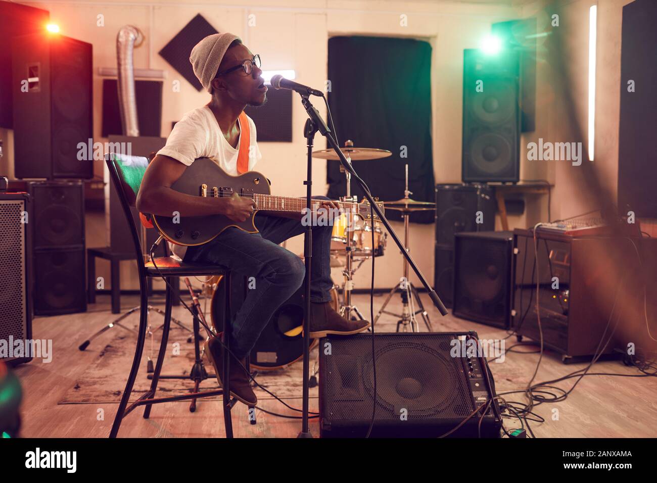 A piena lunghezza Ritratto di contemporaneo afro-uomo cantano al microfono e suonare la chitarra durante le prove o di concerto con la banda musicale in studio di registrazione, spazio copia Foto Stock