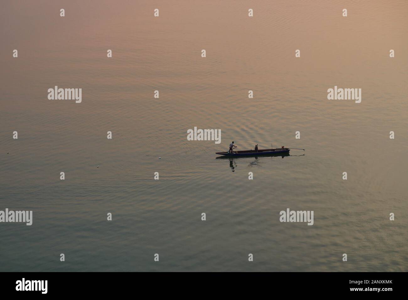 La silhouette del pescatore e una piccola barca da pesca sul fiume Mekong al tramonto, arancio e blu gradiente di colore sulla superficie dell'acqua è ampia Foto Stock