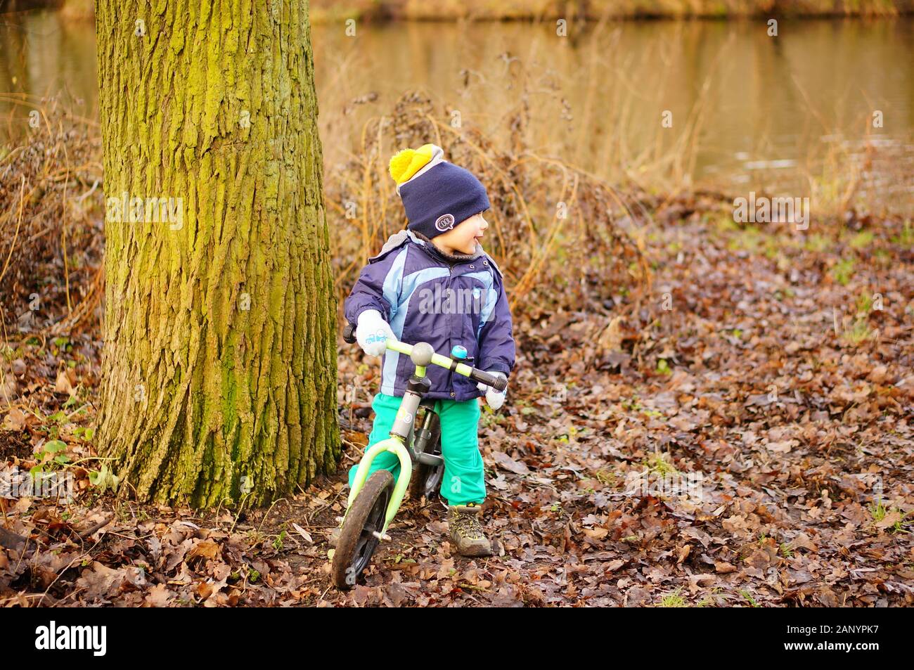 Poznan, POLONIA - 12 gennaio 2020: Giovane ragazzo seduto su una piccola bici da corsa accanto ad un albero vicino a un lago nella foresta di Debiec. Foto Stock