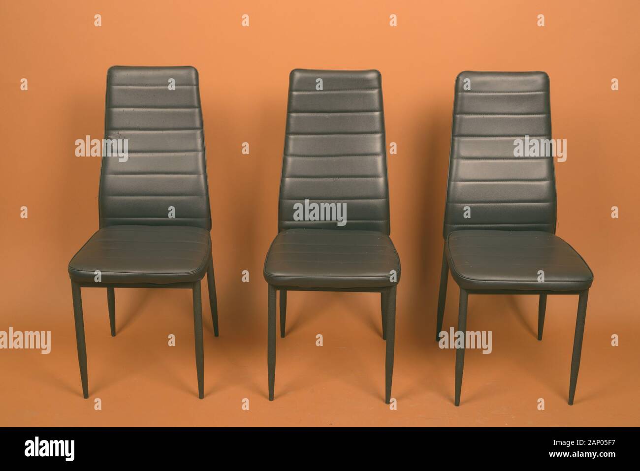 Tre sedie in pelle allineati contro sfondo marrone Foto Stock