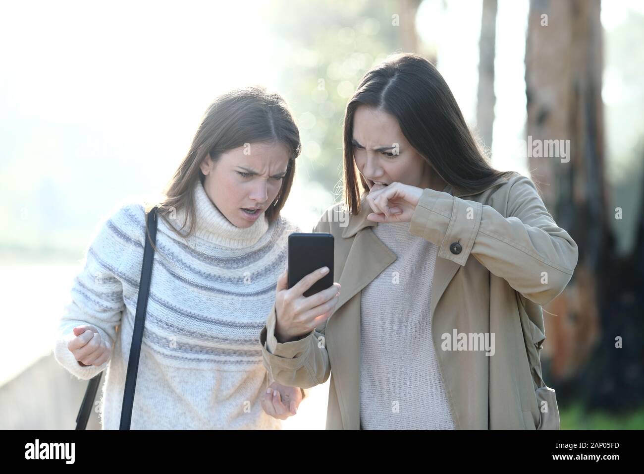 Vista frontale ritratto di due donne arrabbiato controllo mobile phone news in un parco Foto Stock